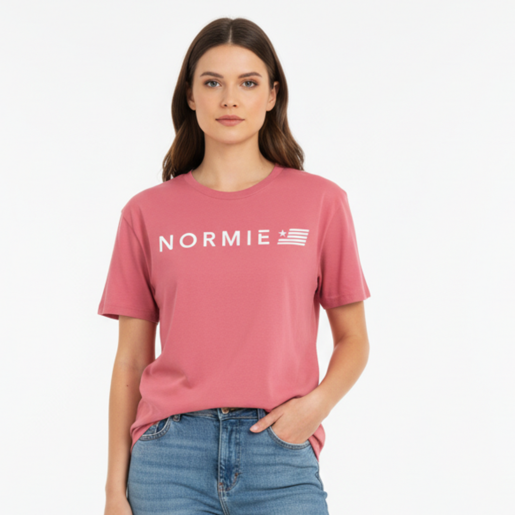 Woman wearing a pinkish red 'NORMIE' t-shirt and blue jeans on a white background